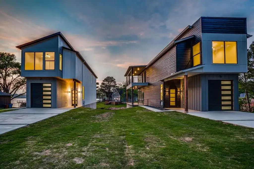 Two contemporary homes with tall windows illuminated at dusk