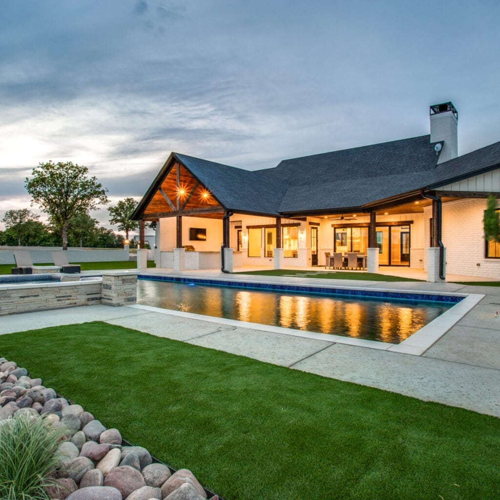 Ranch home at dusk with a covered rear porch, rectangular pool and landscaped yard