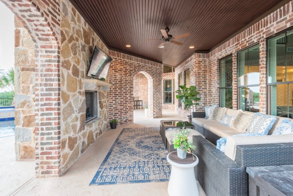 Covered outdoor living room with a stone fireplace and wood ceiling