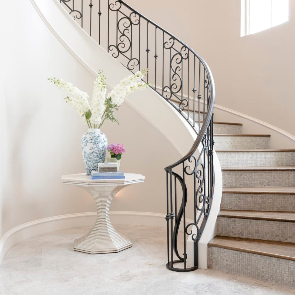 Curved staircase with decorative iron railing in a light-filled entry
