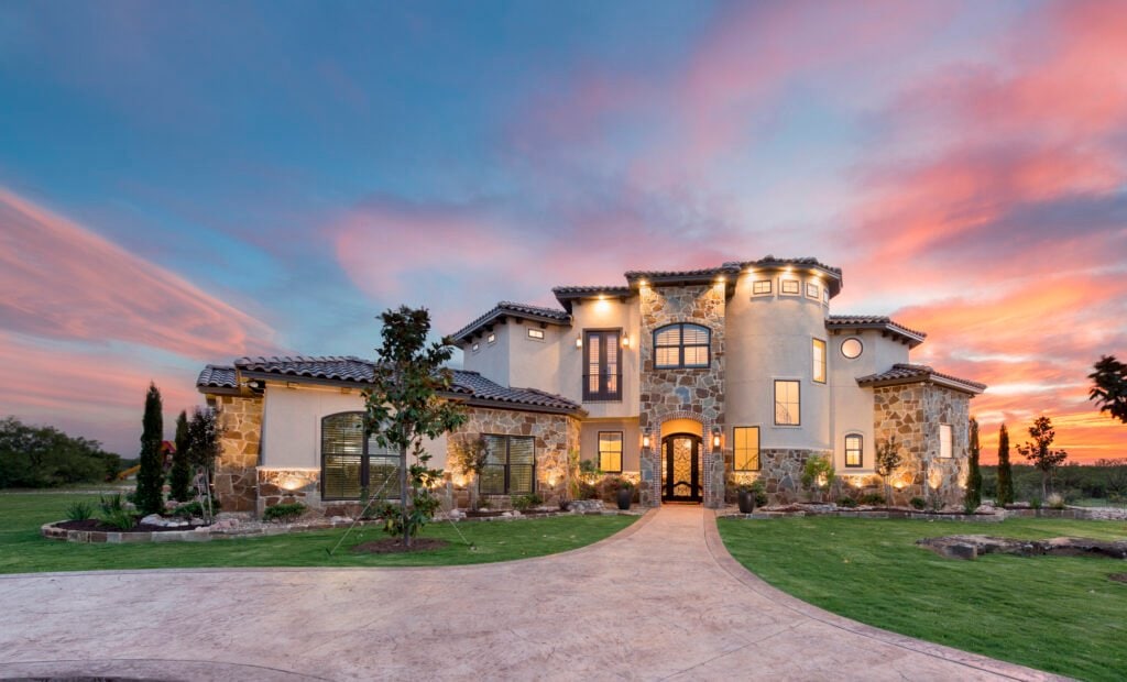 Stone and stucco custom home with a landscaped front courtyard at sunset